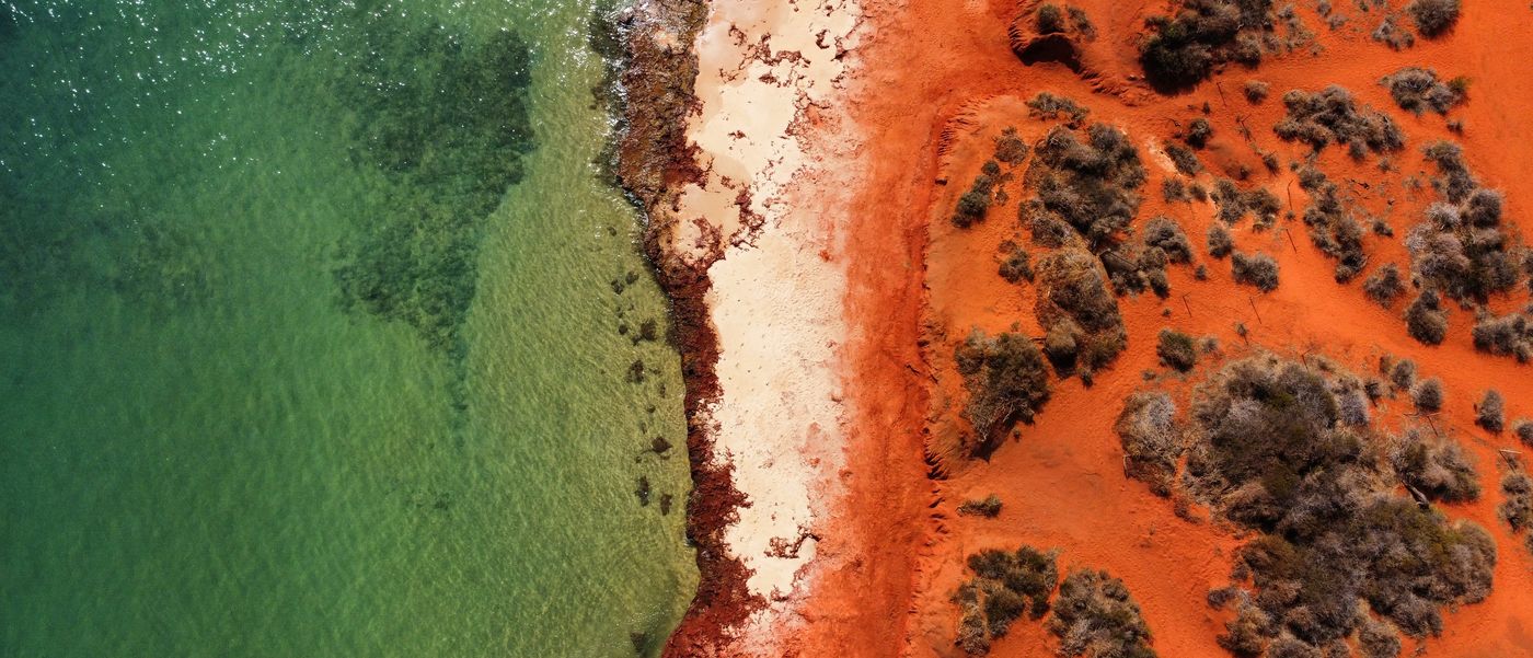Aerial view of the Western Australian coastline where red earth meets clear water.